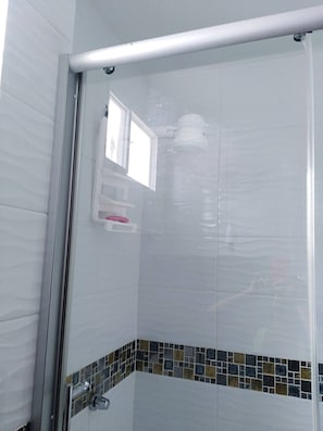 A shower with a glass door, a small window, and a tiled floor with a decorative border. - La Casa Ideal para tus Vacaciones en Playas. Somos tu casa alojamiento temporal. (general villamil playas)