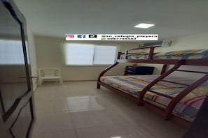 Une chambre avec un lit superposé, une petite chaise blanche, une fenêtre avec des stores et un bureau avec un ordinateur.