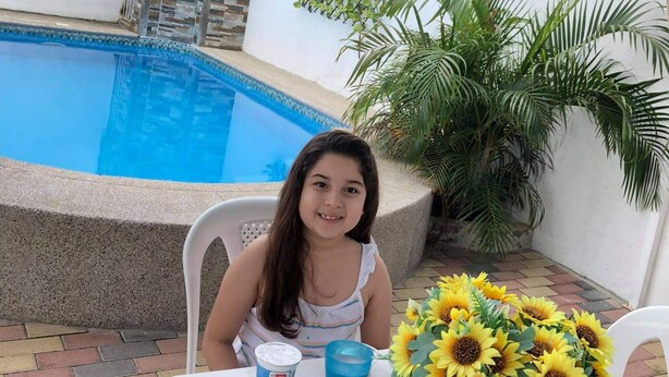 Una persona sentada a una mesa con una piscina al fondo.