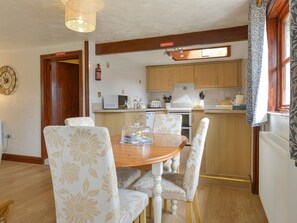 Ein Essbereich mit Holztisch und stuhlförmigen Sitzgelegenheiten mit Blumenmuster, eine Küche mit Holzausbau, einer Uhr und einem Feuerlöscher.