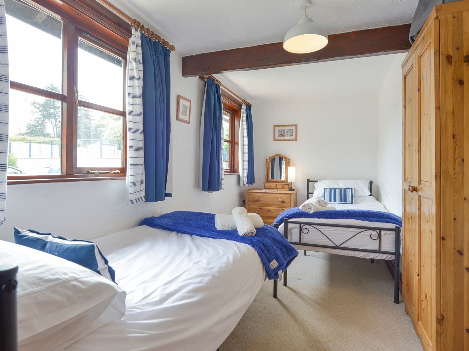 Une chambre avec deux lits, des poutres en bois, une commode et une fenêtre avec des rideaux.