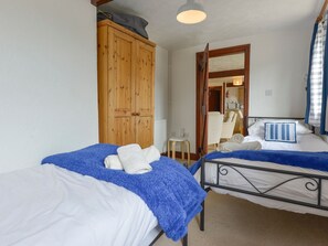 Ein Schlafzimmer mit zwei Betten, einem Holzschrank und einem durchgehenden Türrahmen einsehbarer Badezimmer.