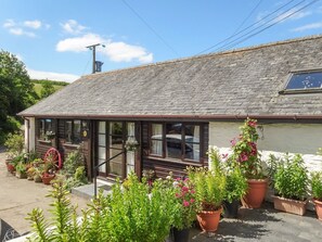 A rustic building with a sloped roof, large windows, and a small porch area with potted plants. - Pillhead Cart Linhay (Bideford)