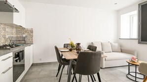 A modern kitchen with a dining area, a sofa, and a small table with flowers. - Quent' home - À 15 min de la plage (Creully sur Seulles)