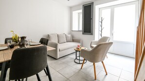 A modern living room with a sofa, chairs, a dining table, and a large window. - Quent' home - À 15 min de la plage (Creully sur Seulles)