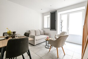 Ein modernes Wohnzimmer mit einer Couch, Sesseln, einem Esstisch und einem großen Fenster.