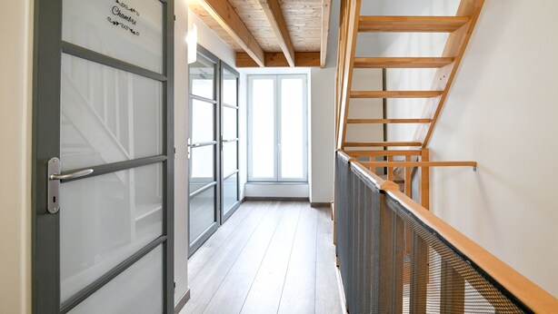 A corridor with a wooden staircase, a door with frosted glass panels, and a view of a bright room. - Quent' home - À 15 min de la plage (Creully sur Seulles)