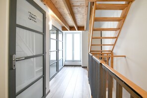 A corridor with a wooden staircase, a door with frosted glass panels, and a view of a bright room. - Quent' home - À 15 min de la plage (Creully sur Seulles)