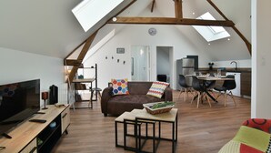 Un salon aménagé dans un style mansardé, avec un téléviseur, un canapé et un coin repas.
