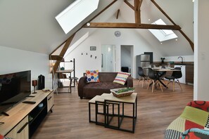 Ein Dachbodenwohnzimmer mit Fernseher, Sofa und Essbereich.