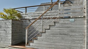 Un escalier en bois avec une rampe métallique menant à une zone abritée.