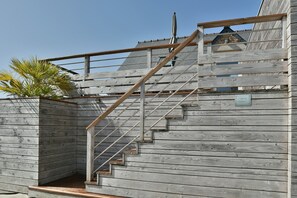 Eine Holztreppe mit Metallgeländer führt zu einem überdachten Bereich.