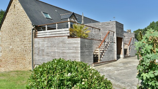 Un bâtiment en pierre avec une extension en bois, un escalier et un ciel dégagé.