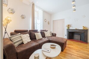 A brown leather sofa with cushions, a white coffee table, a floor lamp, and a fireplace. - La Motte Forte - Jolie maison en centre médiéval (Arnay-le-Duc)
