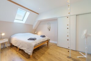 A bedroom with a skylight, a bed, a bedside table with a lamp, a wardrobe, and a standing fan. - La Motte Forte - Jolie maison en centre médiéval (Arnay-le-Duc)