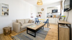 A modern living room with a sofa, coffee table, and chairs, a kitchen area with a microwave, and a dining table with chairs. - Grain de corail - Bel appt à 2 pas de la plage (Pléneuf-Val-André)