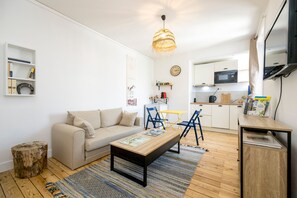 A modern living room with a sofa, coffee table, and chairs, a kitchen area with a microwave, and a dining table with chairs. - Grain de corail - Bel appt à 2 pas de la plage (Pléneuf-Val-André)
