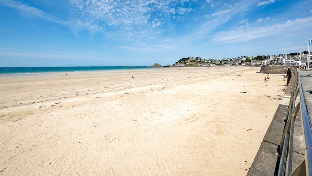 A wide sandy beach with a clear sky, a distant hill, and a few buildings in the background. - Grain de corail - Bel appt à 2 pas de la plage (Pléneuf-Val-André)