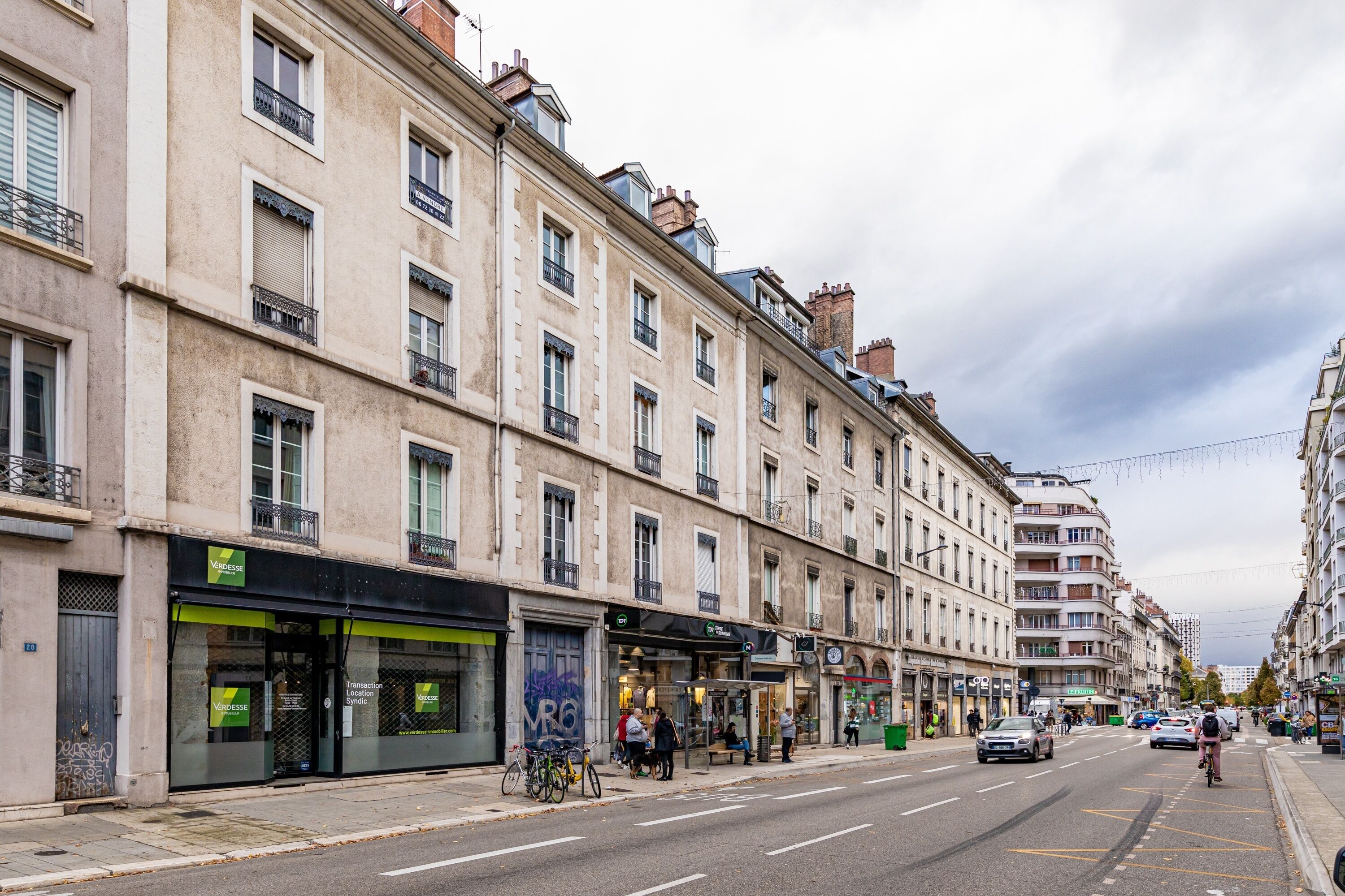 Une rue bordée d’immeubles, avec un arrêt de bus et un panneau indiquant un point de rassemblement en cas d’urgence (VRO).