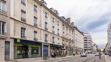 Une rue bordée d’immeubles, avec un arrêt de bus et un panneau indiquant un point de rassemblement en cas d’urgence (VRO).