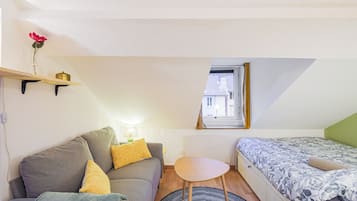Une pièce de taille modeste, comprenant un canapé, une petite table, un lit, une fenêtre et un radiateur.