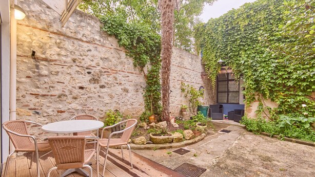 Un patio con mobili in vimini, un muro in pietra e un'area giardino con piante e un albero.