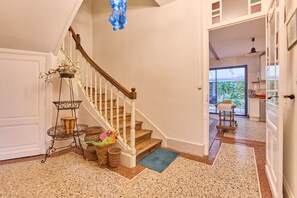 Eine Treppe mit Holzgeländer und weißen Spindeln, die zu einem Raum mit einem großen Fenster und Blick ins Grüne führt.