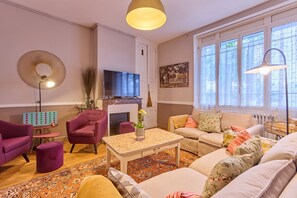 Ein Wohnzimmer mit Kamin, Fernseher und einem großen Fenster mit Vorhängen.