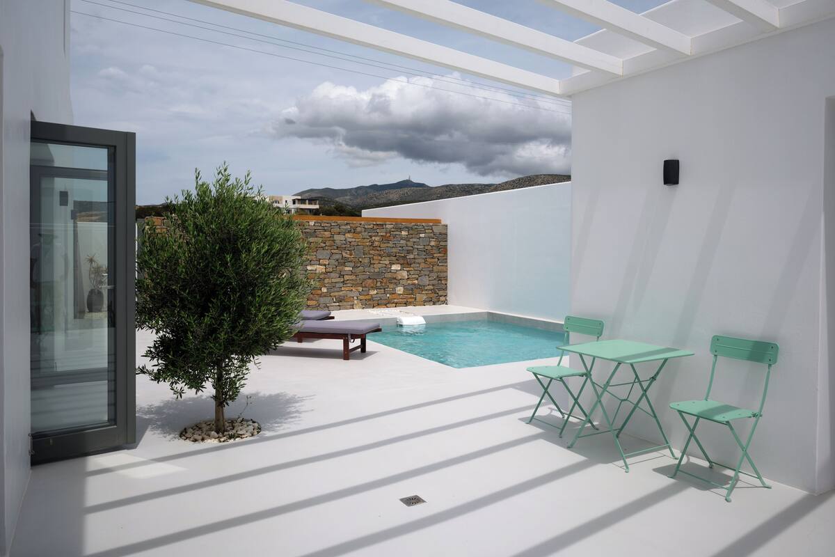 A modern outdoor pool area with a stone wall, a small tree, and two green chairs.