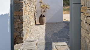 A narrow pathway with a stone wall on one side and a white wall on the other, leading to a door. - Villa Iliada - Paros Escape (Paros)