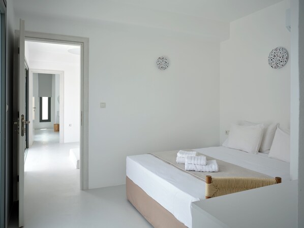 A bedroom with a bed, a door leading to another room, and a wall-mounted light fixture. - Villa Iliada - Paros Escape (Paros)