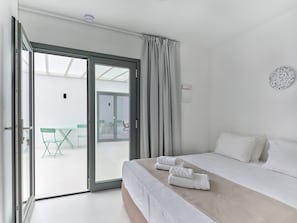 Une chambre d’hôtel avec un lit, une vue sur un espace extérieur aménagé accessible par une porte-fenêtre coulissante, et un luminaire fixé au mur.