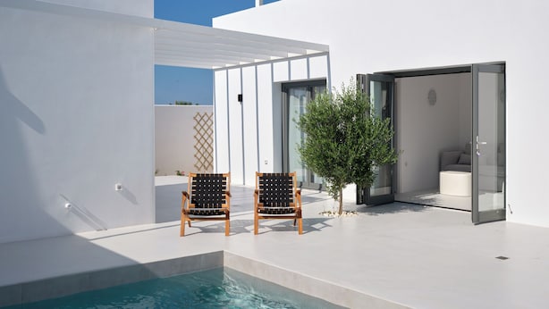 A modern pool area with two wooden chairs, a glass door leading to a room, and a clear blue sky. - Villa Iliada - Paros Escape (Paros)