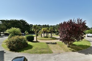 A landscaped area with various trees and shrubs, a paved path, and a parked car. - Le Palais des Arcades - Studio 100m de la Plage (Fréhel)