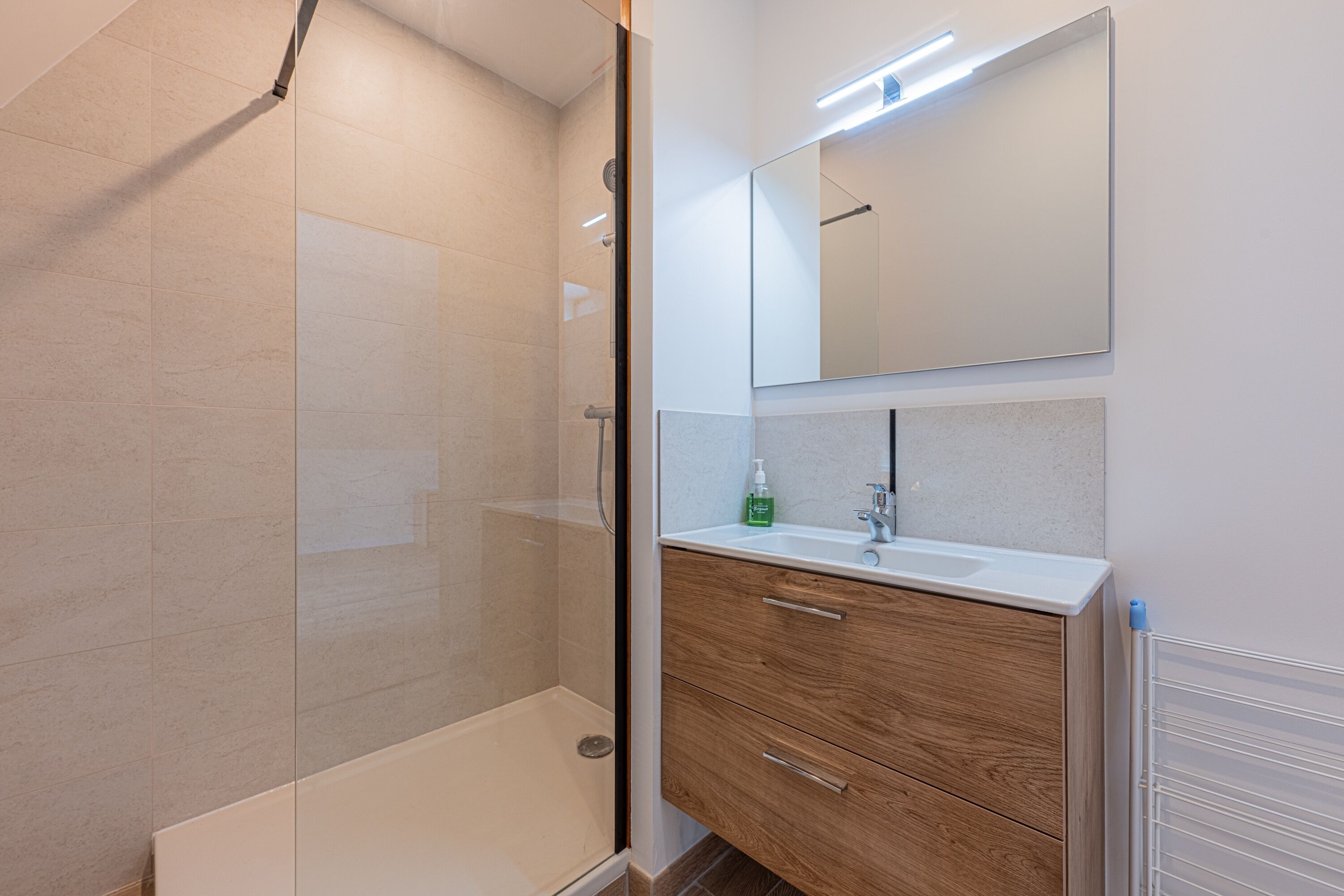 A modern bathroom with a glass shower enclosure, a wooden vanity, and a large mirror.