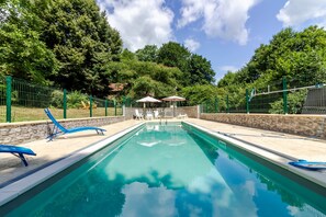 A swimming pool with lounge chairs and umbrellas, surrounded by a stone wall and greenery. - La Parenthèse Fleurie - Avec Piscine Privée (Saint-Priest-les-Fougères)