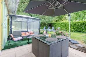 A covered patio area with a glass enclosure, outdoor seating, and a large umbrella.