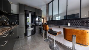 Et moderne køkken med mørke skabe, en backsplash med sorte fliser og to barstole med træsæder.
