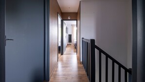 En gang med trægulv, gelænder i sort og en loftlampe.
