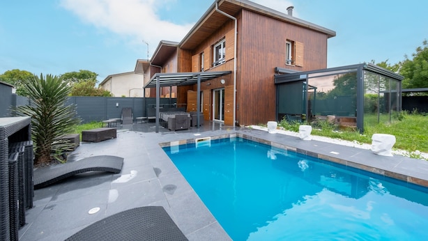 Et moderne hus med swimmingpool, udendørs møbler og en overdækket patio.