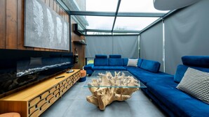 En moderne stue med sofabord i glas, blå sofa, sidebord i træ og et vægmonteret fladskærms-tv.