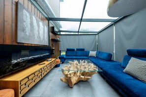A modern living room with a glass coffee table, blue sofa, wooden side table, and a mounted flat-screen TV. - La Villa Rosa - Avec Piscine Privée (Toulouse)