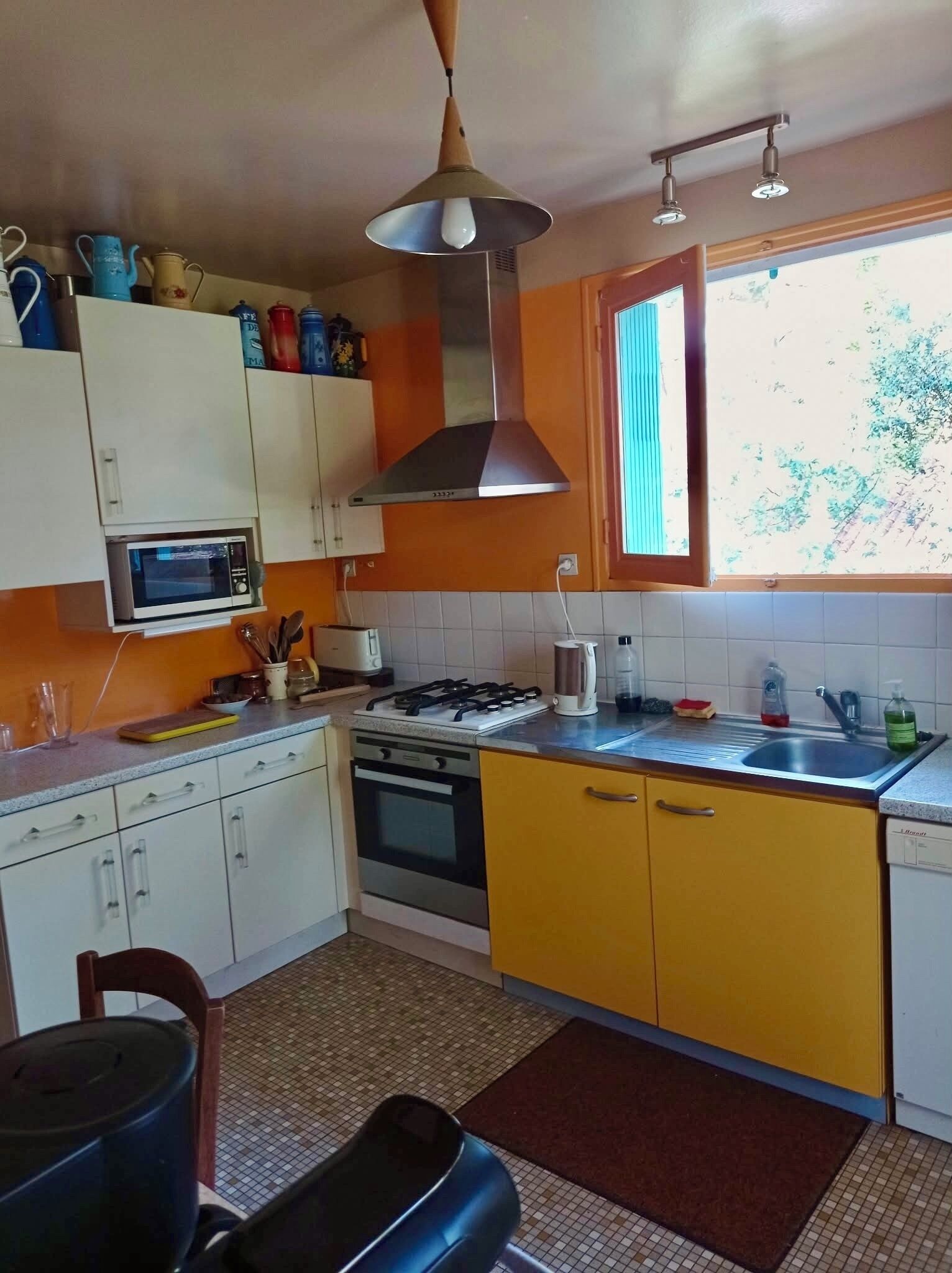A kitchen with white and yellow cabinets, a gas stove, a microwave, and a window with a view of trees.