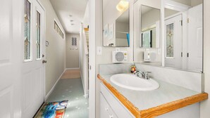 Een badkamer met een witte wastafel, een grote spiegel en een deur met een decoratief glasraam.
