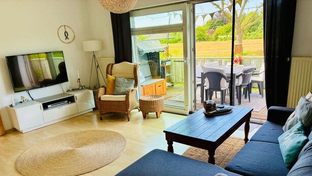 A living room with a sofa, a TV, a coffee table, and a dining area with chairs and a table. - Vacation apartment DE VRIESenkoje (Südbrookmerland)