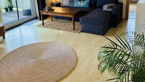 A modern living room with a sofa, coffee table, and a large woven rug. - Vacation apartment DE VRIESenkoje (Südbrookmerland)