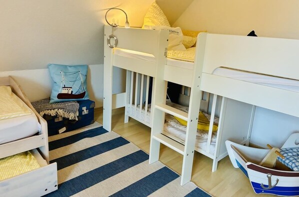 Un lit superposé pour enfant avec une tête de lit en forme de bateau, un tapis à rayures et une petite valise bleue.