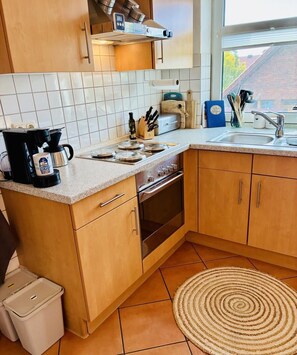 Une cuisine avec des meubles en bois, une cuisinière, une machine à café et une fenêtre donnant sur un immeuble.