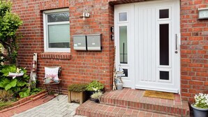 A brick house with a white door, a small porch, and a welcome mat. - Vacation apartment DE VRIESenkoje (Südbrookmerland)