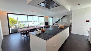 Una cocina moderna con una isla grande, un comedor con mesa y sillas, y vistas amplias a través de grandes ventanales.